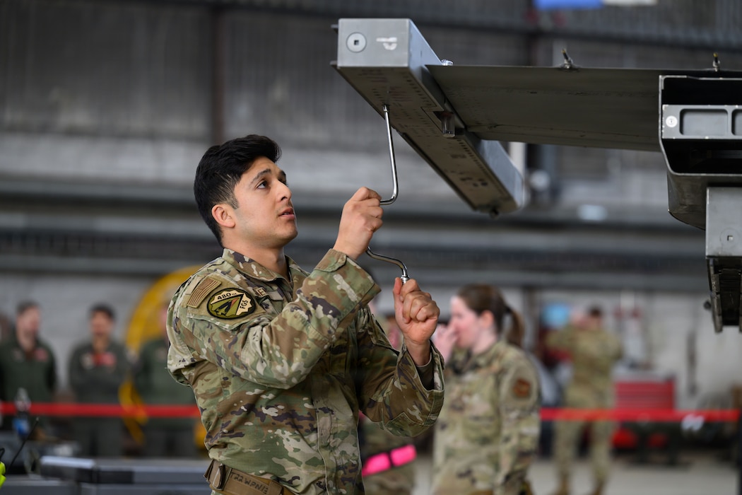 A person loosens screws underneath the wing tip of a fighter aircraft to prepare it for a missile to be mounted.