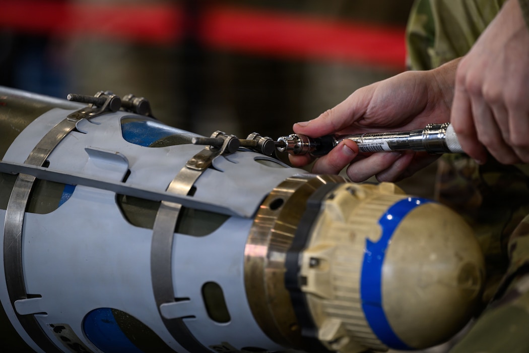 A person uses a tool to tighten a metal clip around a bomb.