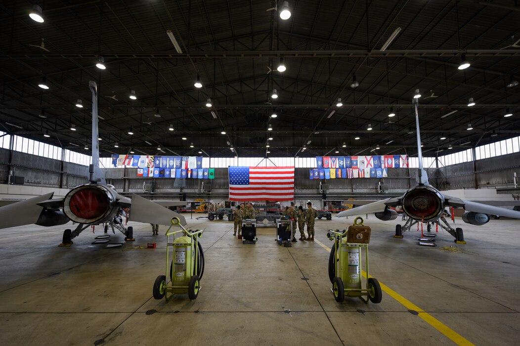 Two teams of people prepare for a competition in between two fighter aircraft inside an aircraft hangar.