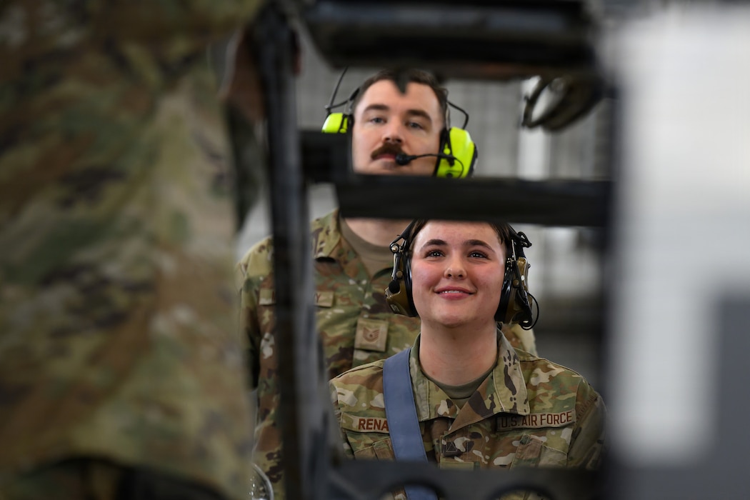 Two people look watch a person load a weapon onto an aircraft.