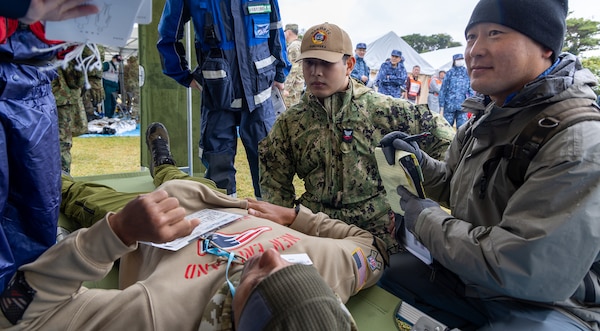 JOGASHIMA PARK, Japan (Nov. 9, 2025) — A U.S. Navy Hospital Corpsman assigned to U.S. Navy Medicine Readiness and Training Command Yokosuka assists Japanese emergency personnel in stabilizing a simulated casualty during Big Rescue Kanagawa 2025. The annual exercise is one of Kanagawa Prefecture’s largest disaster-response drills, involving U.S. Naval Hospital Yokosuka, Red Cross Yokosuka and Branch Health Clinic Atsugi personnel working alongside U.S. and Japanese agencies. (U.S. Navy photo by Daniel Taylor/USNMRTC Public Affairs)