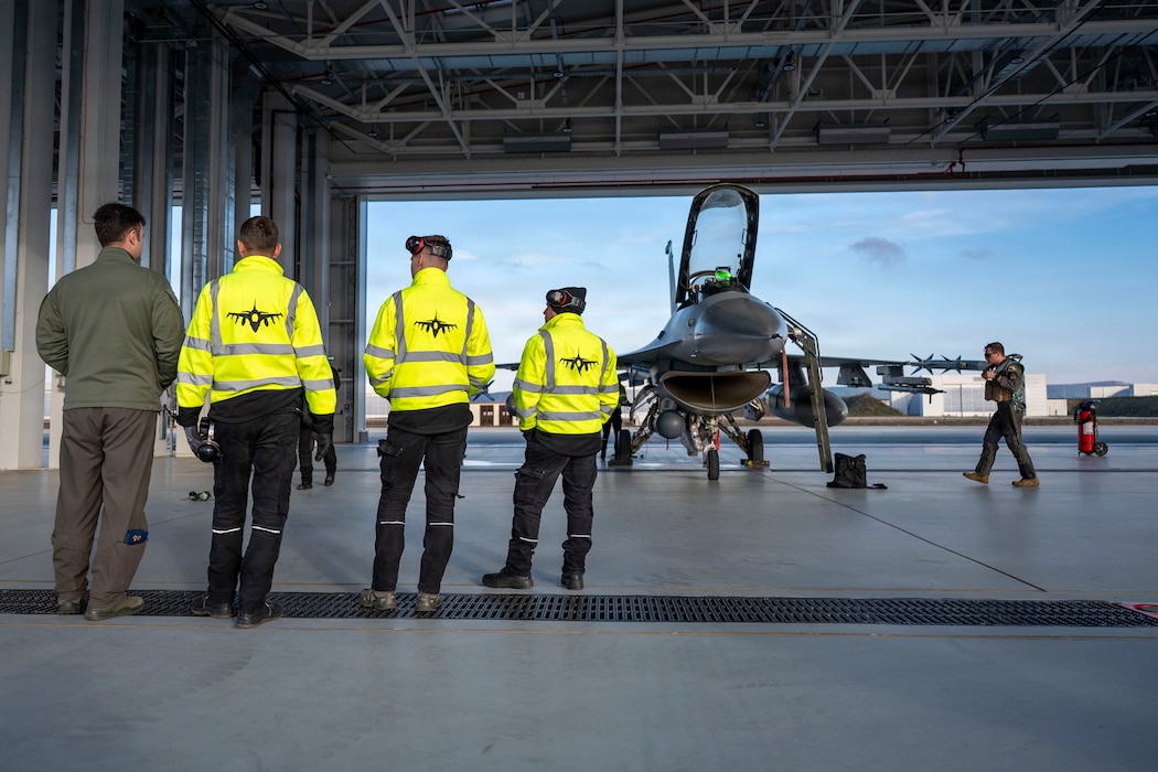 U.S. Air Force Maj. John McGee, 555th Fighter Squadron F-16 Fighting Falcon pilot, walks to an F-16 while Romanian Air Force members watch during routine Agile Combat Employment operations at Campia Turzii, Romania