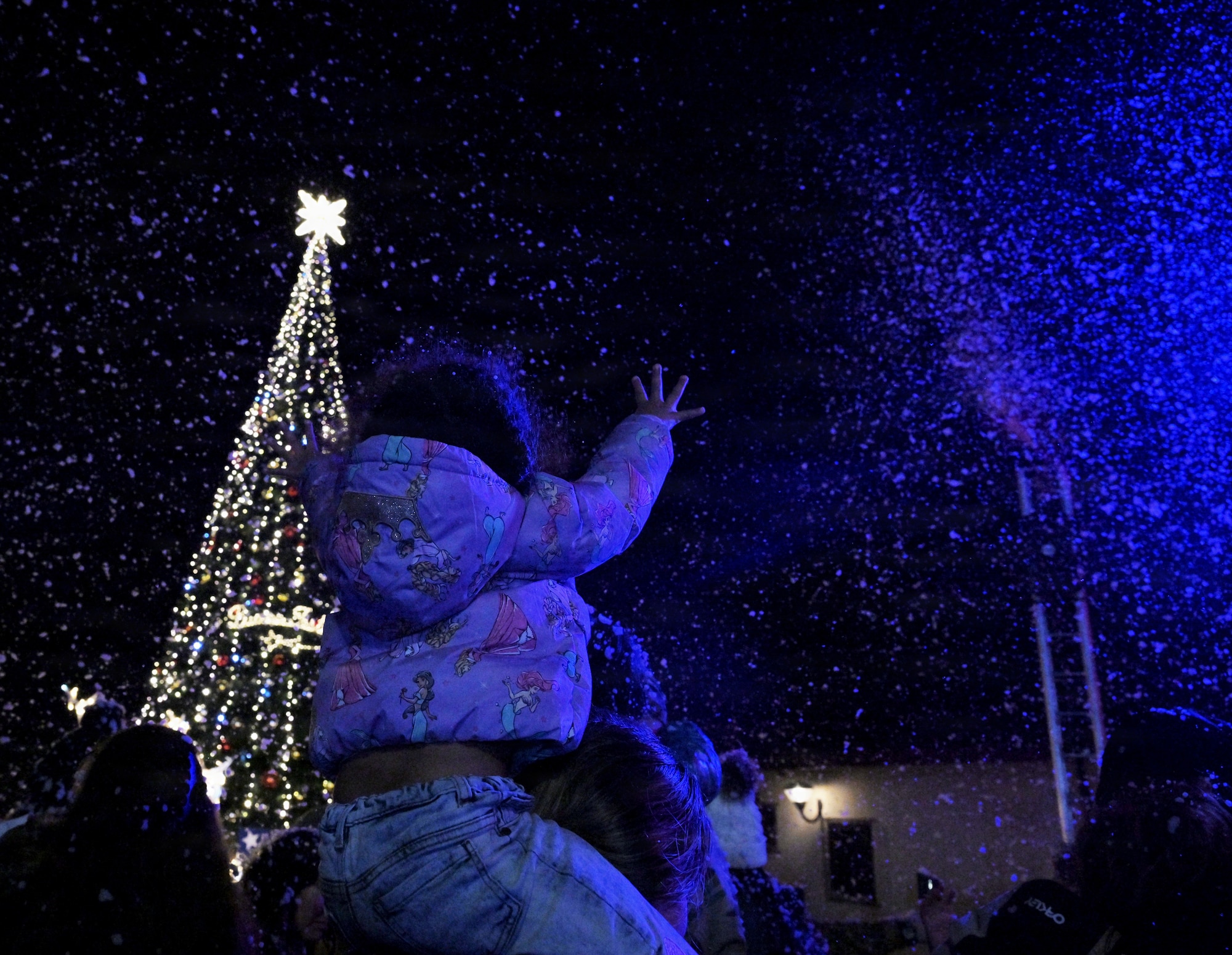 A little girl reaches for the sky during a tree lighting ceremony in artificial snow