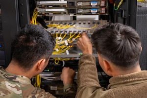 Two Airmen look on and assess a wiring panel.