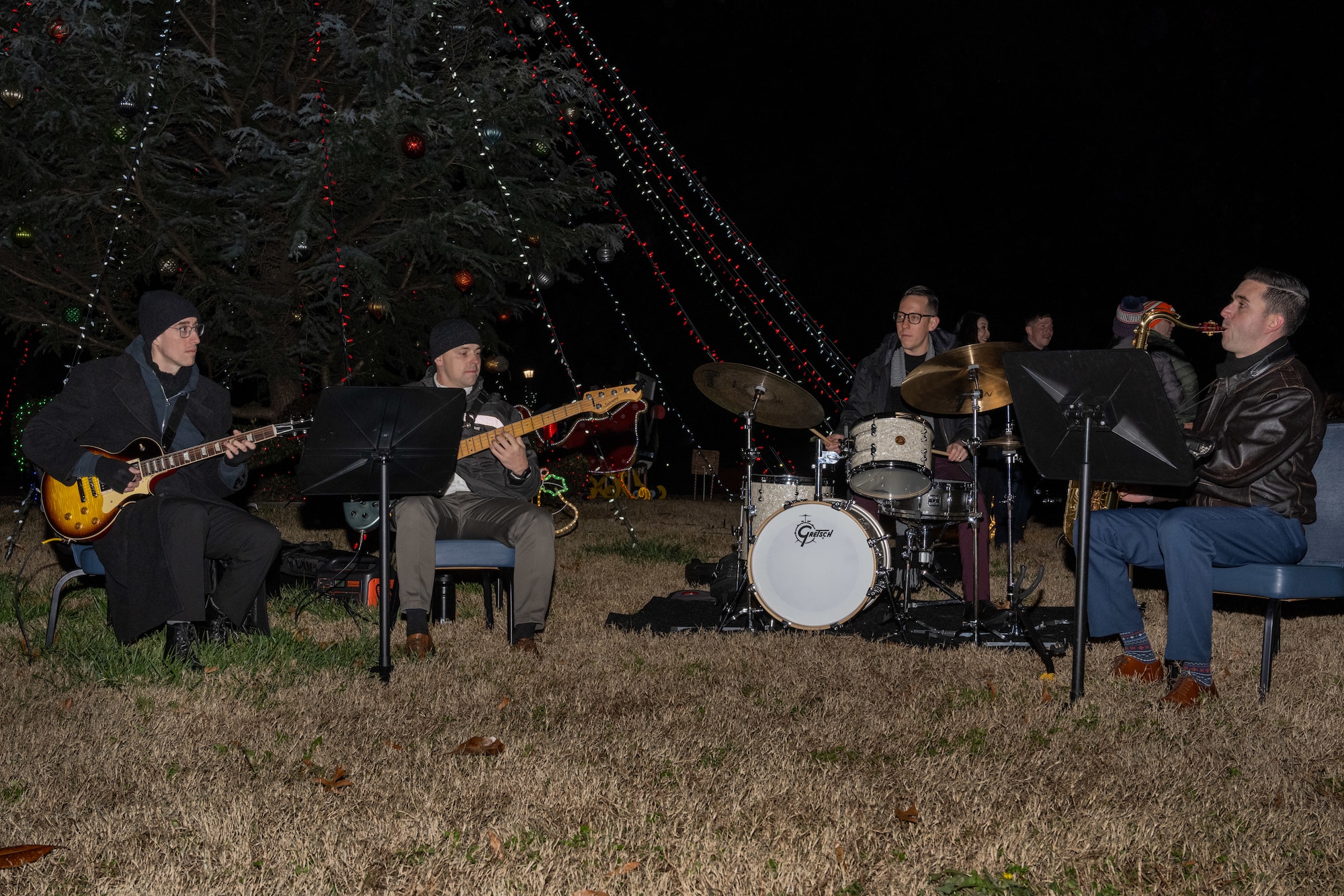 Four men sit in chairs while playing musical instruments.