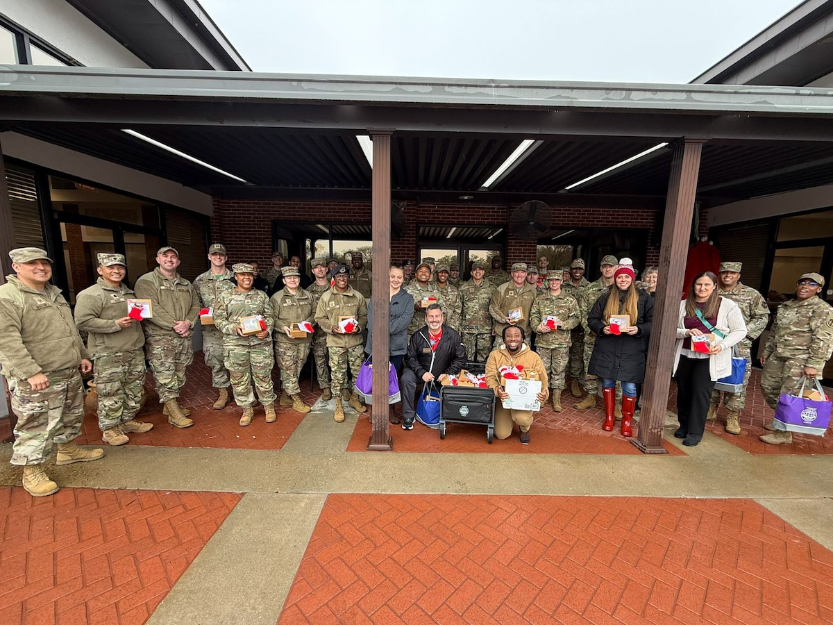 A large group of Airmen and some civilian volunteers pose together while holding boxes of cookies to deliver