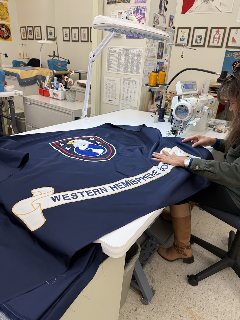 A woman dressed in casual attire guides fabric through a sewing machine.