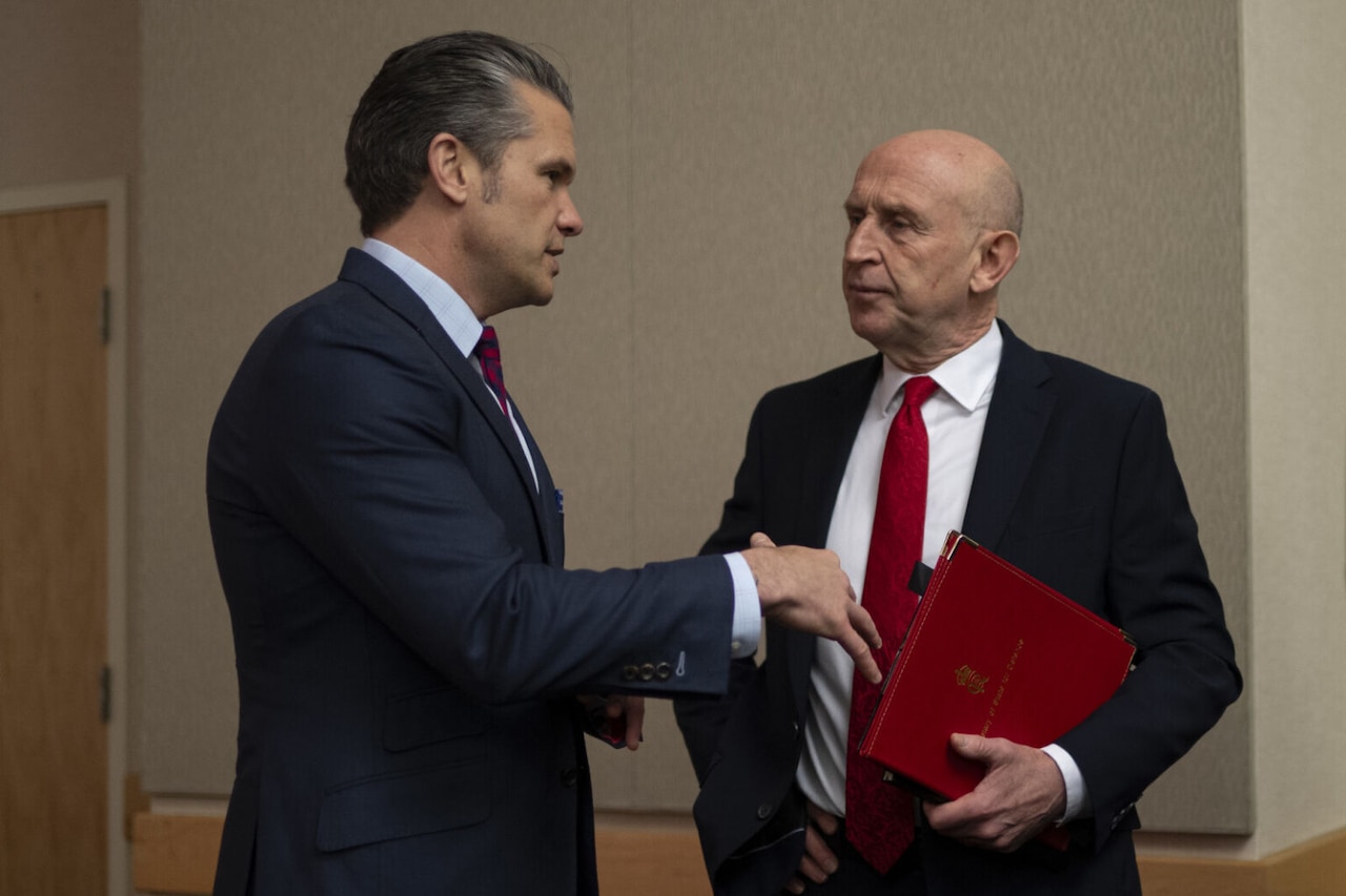 Two men in business attire are standing indoors having a conversation.
