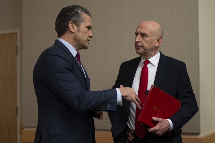 Two men in business attire are standing indoors having a conversation.