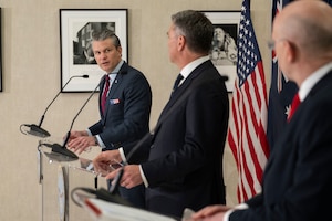 The secretary of war speaks from a podium while looking at two others.