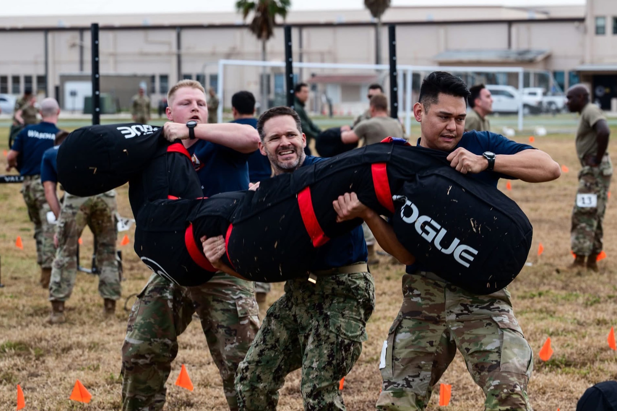 Three men carry large sandbags across a field