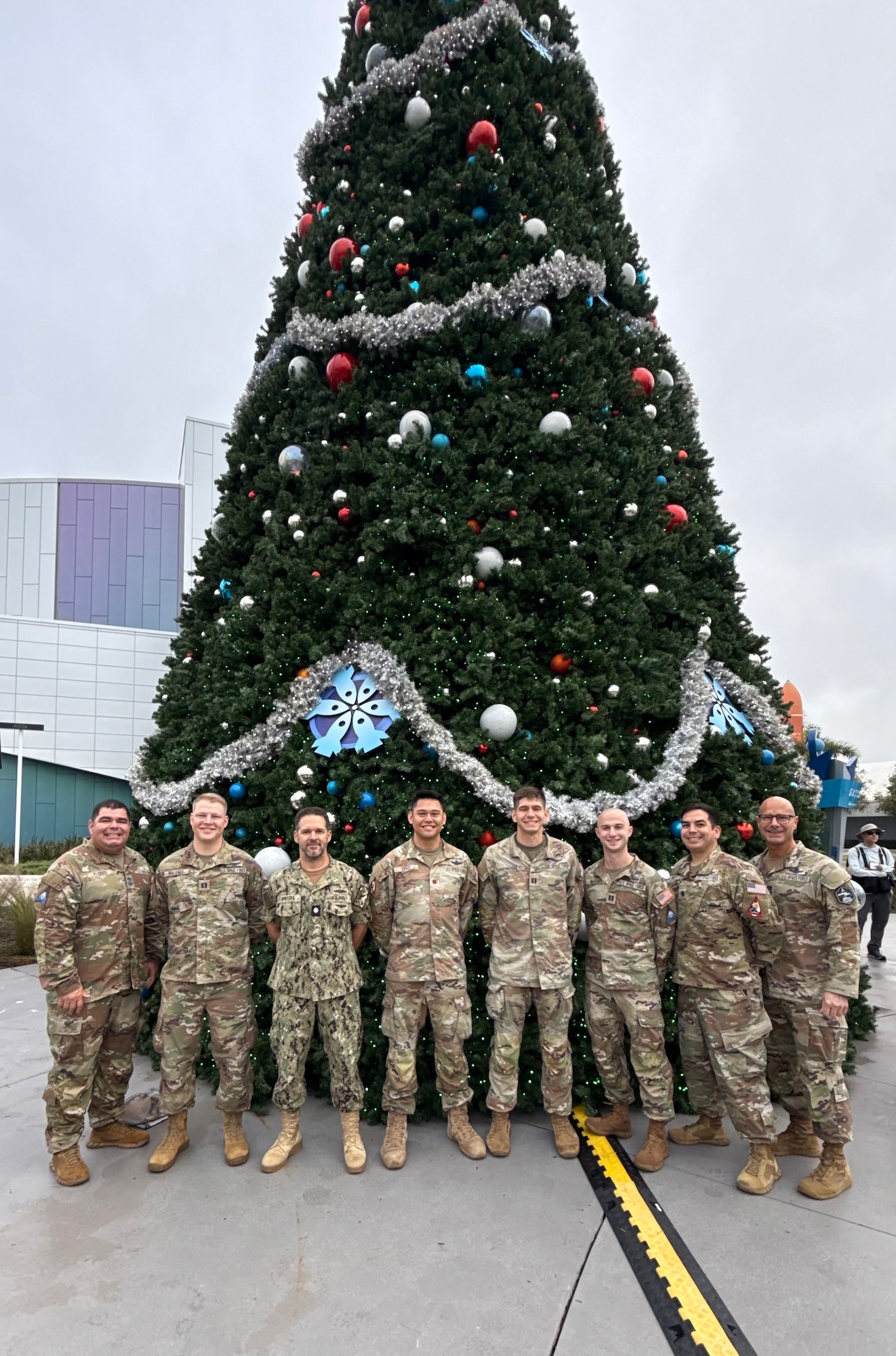 Eight men stand in front of a large decorated christmas tree