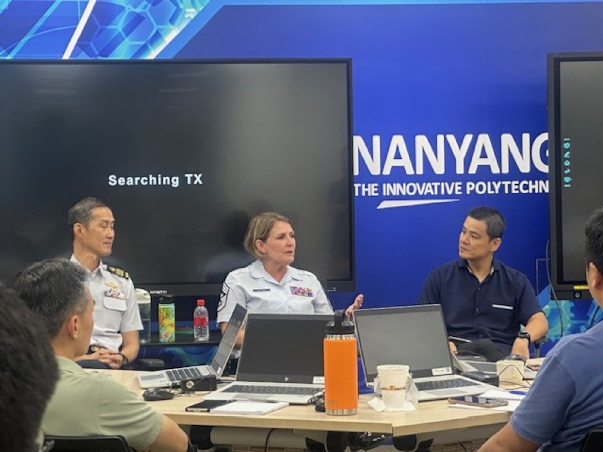 A uniformed woman speaks to several men seated around her in a classroom.