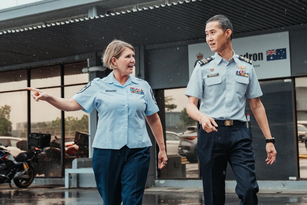 A military uniformed woman points to the side while walking next to military uniformed man.