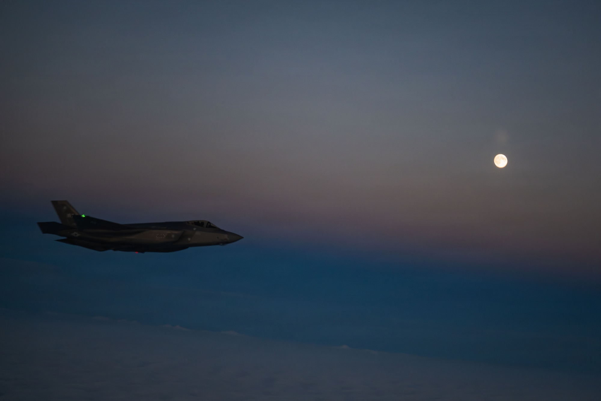 A U.S. Air Force 48th Fighter Wing F-35 Lightning II flies under a moonlit sky beside a 100th Air Refueling Wing KC-135 Stratotanker over the Baltic Sea