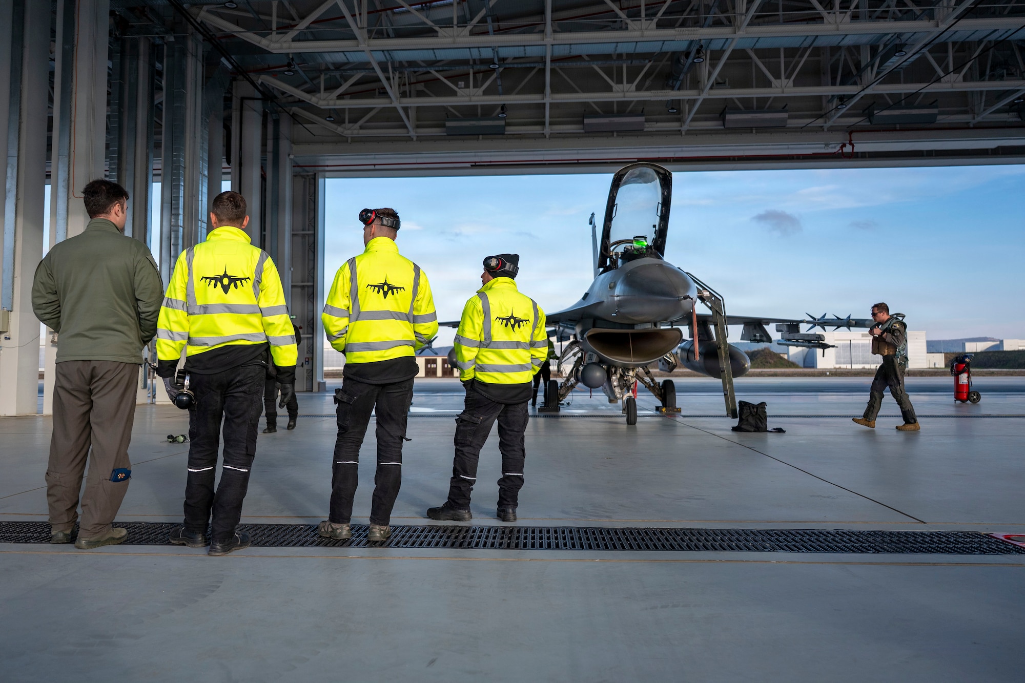 U.S. Air Force Maj. John McGee, 555th Fighter Squadron F-16 Fighting Falcon pilot, walks to an F-16 while Romanian Air Force members watch during routine Agile Combat Employment operations at Campia Turzii, Romania