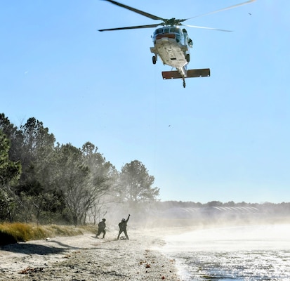 Aircrewmen from the Naval Air Station (NAS) Patuxent River Search and Rescue "SAR Dogs" unit signal to an MH-60S Seahawk helicopter after locating and assessing simulated crash survivors. The scenario was part of the final L00A qualification flight for Hospital Corpsman 3rd Class Arsides Garay, testing the crew’s ability to conduct a successful rescue without specific location data.