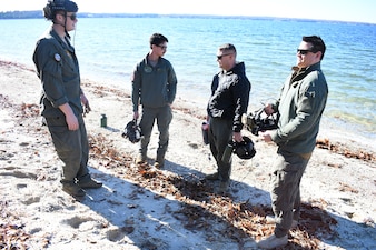 Naval Aircrewmen from the Naval Air Station (NAS) Patuxent River "SAR Dogs" unit prepare a simulated crash site on a beach prior to a rescue evolution. From Left, Naval Aircrewmen (Helicopter) 2nd Class Kanon Brooks, Hospital Corpsman 2nd Class Andrew Conklin, Senior Chief Hospital Corpsman Mackenzie W. Gordon and Naval Aircrewmen (Helicopter) 1st Class Joseph Conant set the stage for a realistic L00A qualification flight. This vital preparation ensures the scenario effectively tests the incoming aircrew's ability to locate, assess, and rescue simulated casualties without prior information.