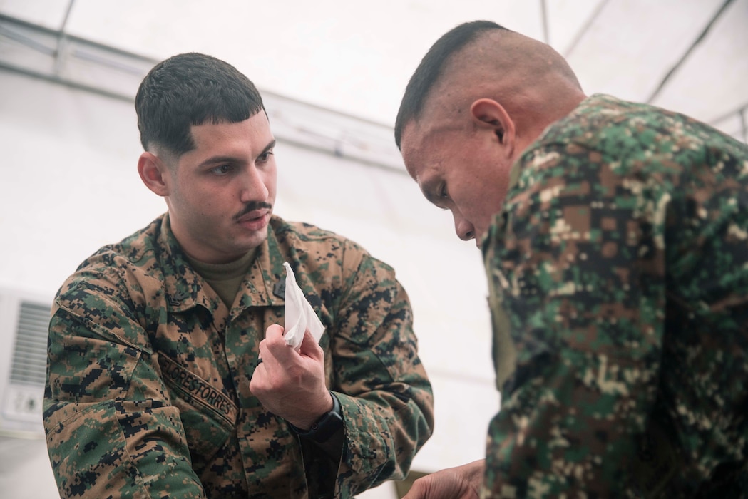 U.S. Navy Hospitalman Second Class Juan Florestorres, assigned to Marine Rotational Force-Southeast Asia, I Marine Expeditionary Force, demonstrates to a Philippine Marine assigned to 3rd Marine Brigade how to properly seal an open chest wound during a tactical combat casualty care subject matter expert exchange as part of exercise Marine Air Support Activity 2025 at Marine Base Camp Rodolfo, Palawan, Philippines, Oct. 13, 2025.  TCCC is a training program for non-medical personnel to have knowledge and skills to render life-saving medical aid in the absence of medical personnel in combat scenarios.  MASA 25 is an annual joint Philippine and U.S. military exercise focused on mutual defense, strengthening relationships, and rehearsing emerging aviation concepts. Florestorres is a native of Florida. (U.S. Marine Corps photo by Sgt. Luis Agostini)