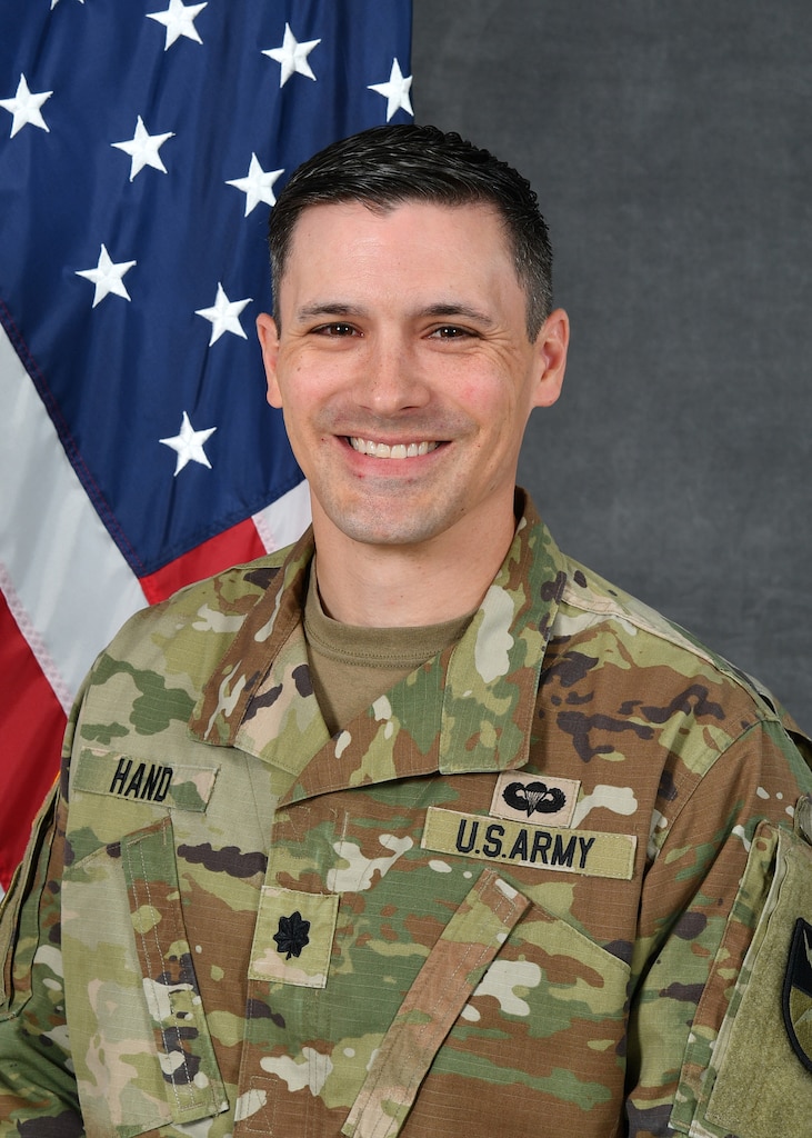 A soldier in uniform sitting in front of an American Flag
