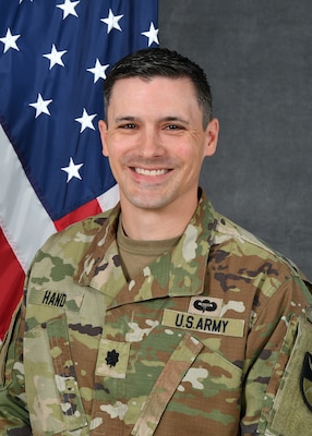 A soldier in uniform sitting in front of an American Flag