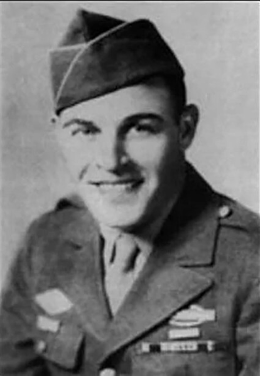 A man in a military uniform and cap smiles for a photo.