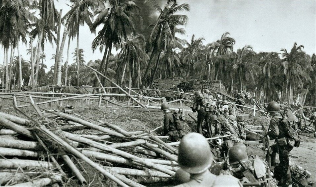 Dozens of men move past fallen trees into a patch of tropical forest.