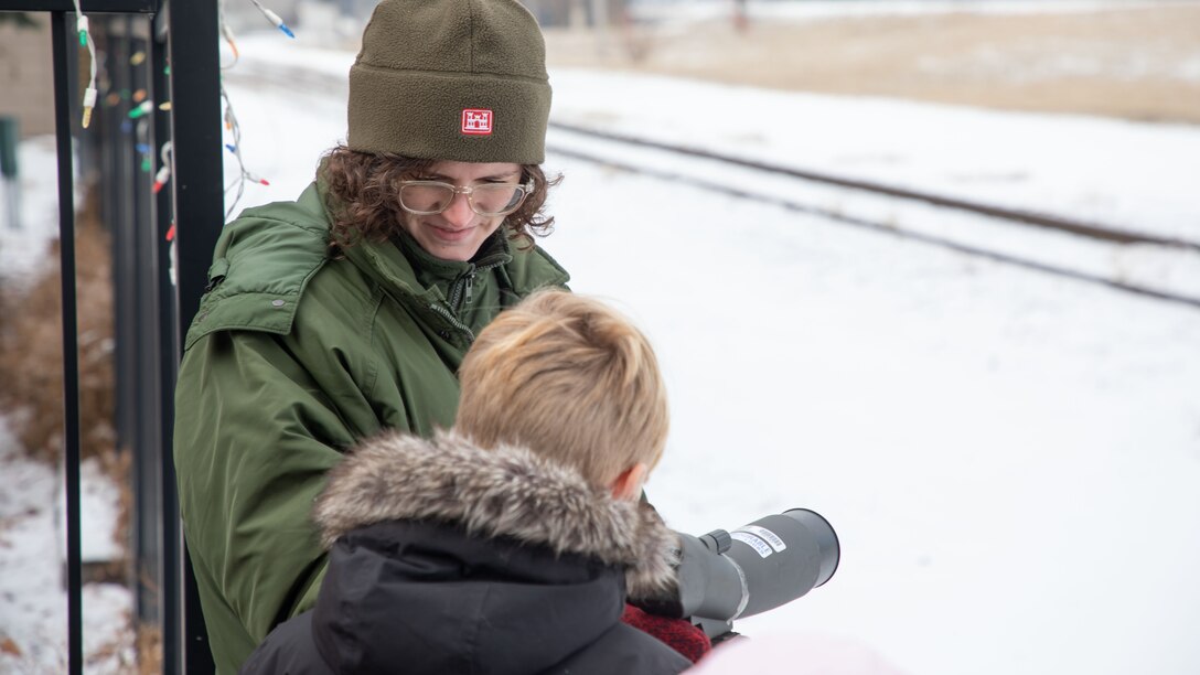 A USACE park ranger helps a young eagle watcher to spot an eagle with a spotting scope.