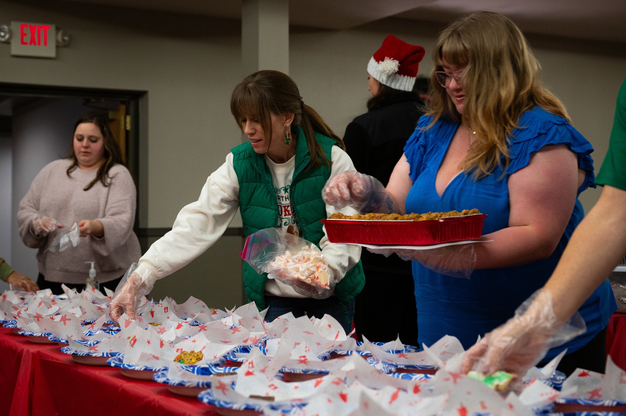 A photo of a group of people sorting out cookies on to plates on a red table.