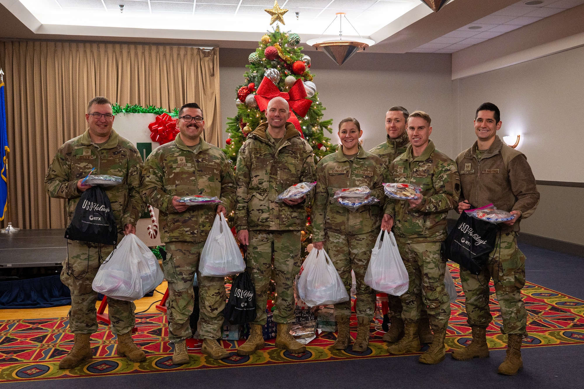 A photo of a group of airmen standing in front of a Christmas tree with bags of cookies in their hands.