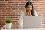 Woman looks at a laptop while she sits at a table.