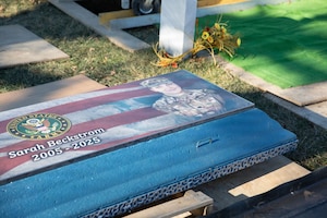 The top of a specialized burial vault lid is shown with an artistic portrait of a woman in a camouflage military uniform and the American flag and Army Seal. Written on the top of the lid is “Sarah Beckstrom, 2005-2025.”