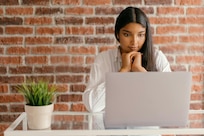 Woman looks at a laptop while she sits at a table.