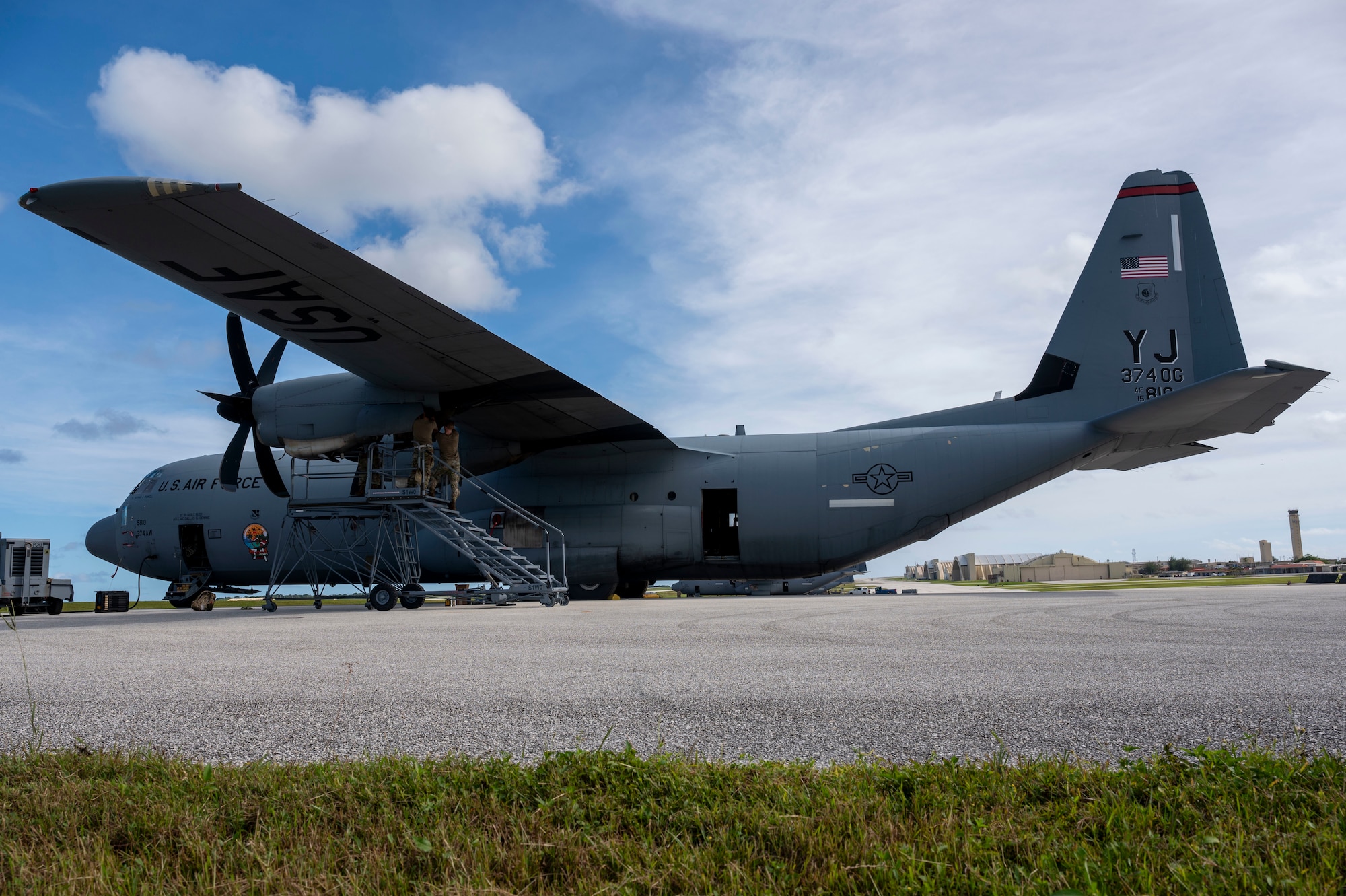 Three military members conduct maintenance work on a C-130J aircraft.