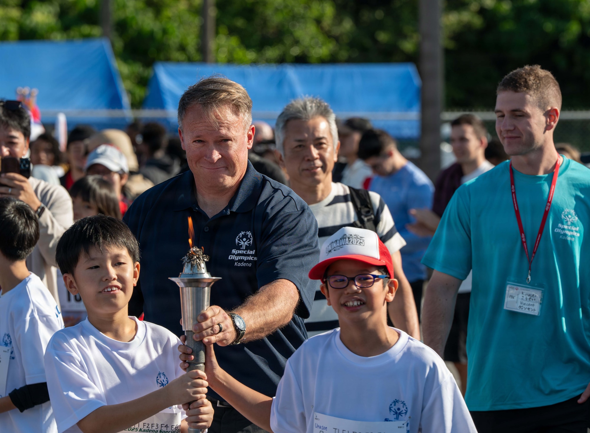 U.S. Air Force Chief Master Sgt. William Cupp, 18th Wing command chief, and Special Olympics athletes carry the torch to commence the beginning of the 2025 Kadena Special Olympics at Kadena Air Base, Japan, Dec. 6, 2025. KSO is an annual sporting event hosted by the 18th Wing that uplifts Okinawan and American athletes with physical and intellectual disabilities.  (U.S. Air Force photo by Staff Sgt. Gary Hilton)
