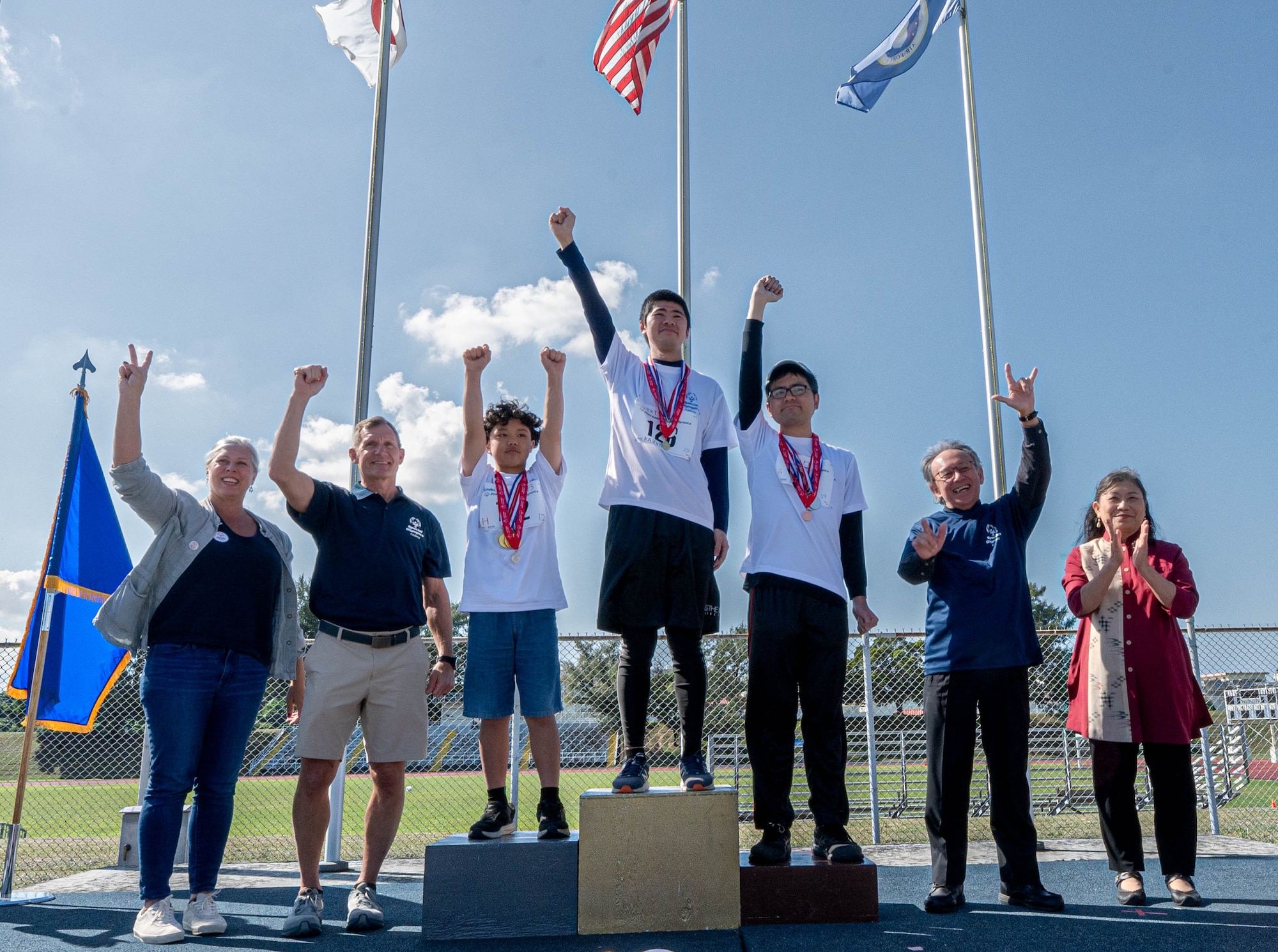 Okinawa Governor Denny Tamaki, right, joins U.S. Air Force Brig. Gen. John Gallemore, 18th Wing Commander, in celebrating Kadena Special Olympics 100-meter dash winners at Kadena Air Base, Japan, Dec. 6, 2025. Hundreds of volunteers with the Department of War, Japan Air Self Defense Force, and local community worked tirelessly to ensure the success of the event over a six-month period. The volunteers helped in a variety of duties including translation, food preparation, logistical and medical support, security and assisting as athlete buddies. (U.S. Air Force photo by Airman 1st Class Arnet Tamayo)