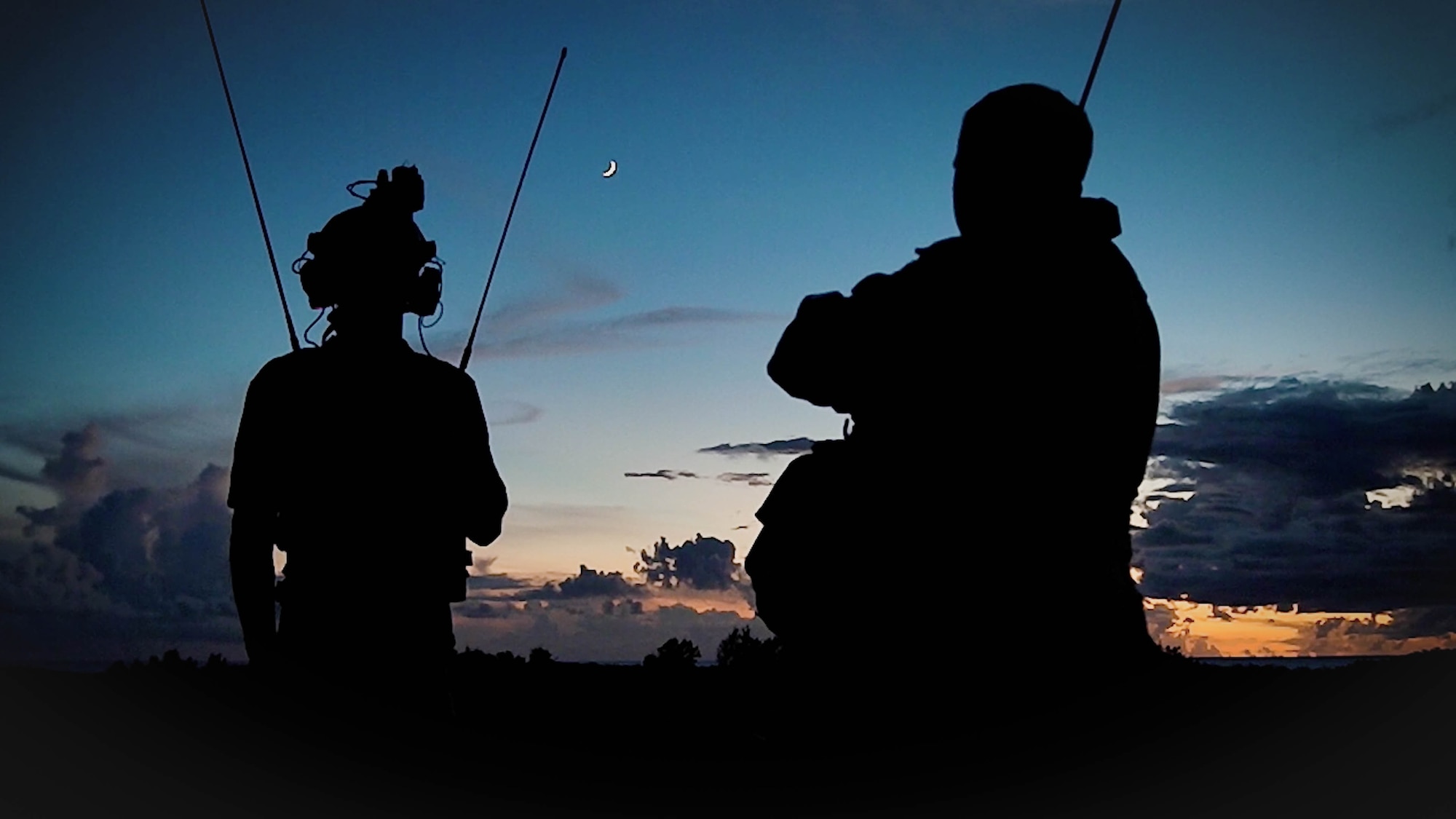 The silhouettes of landing zone safety officers outline a sunset
