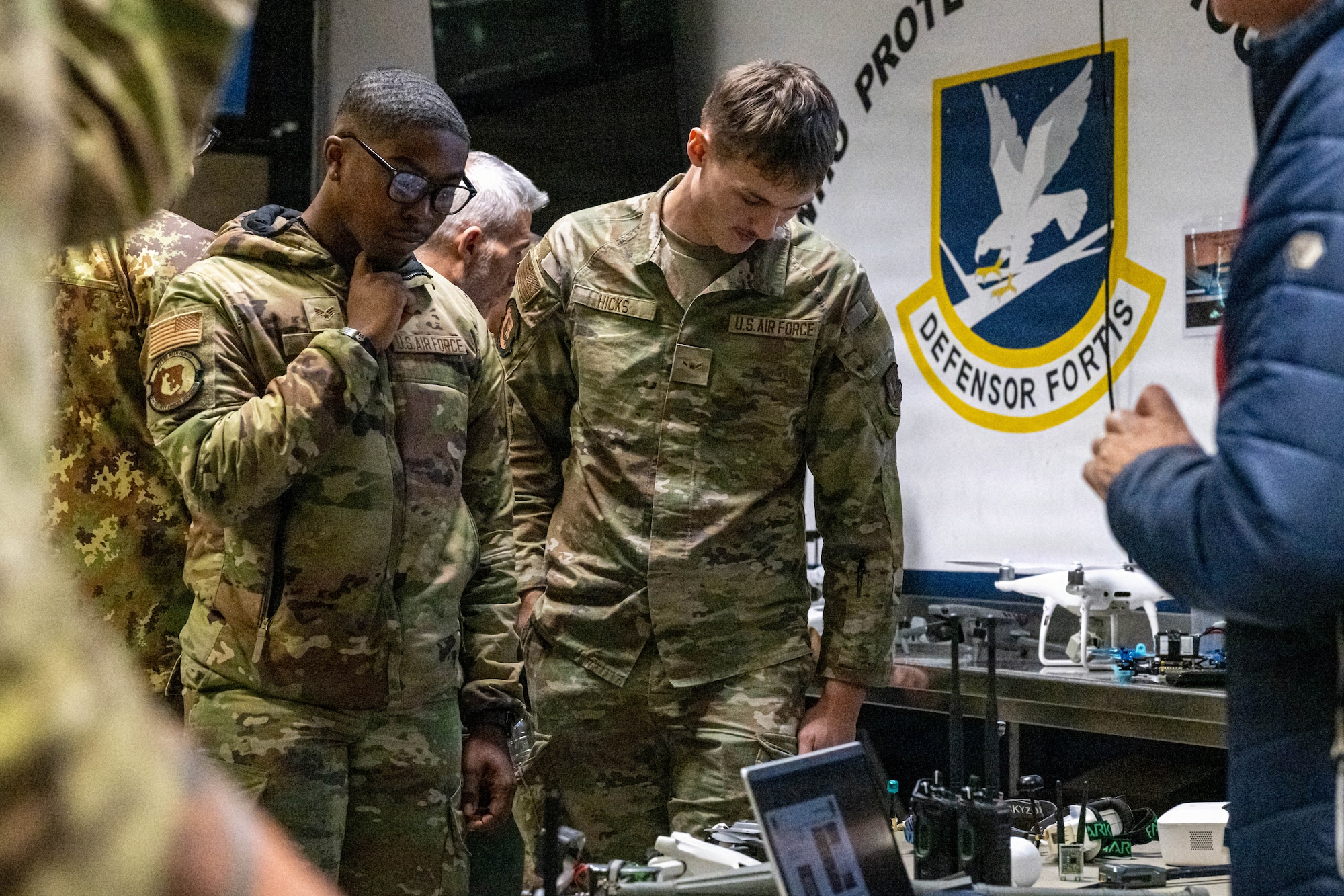 Two airmen stand side-by-side and look at drones.