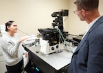 JOINT BASE SAN ANTONIO-FORT SAM HOUSTON (Dec. 8, 2025) Research scientist Phylisia Dimas, assigned to Naval Medical Research Unit (NAMRU) San Antonio, speaks with Dr. Jeremy Pamplin, program manager, Biological Technologies Office, Defense Advanced Research Projects Agency (DARPA), on the Nikon Eclipse Ti2 confocal microscope utilized for the assessment of DARPA’s Fieldable Solutions for Hemorrhage with bio-Artificial Resuscitation Products (FSHARP) program’s novel synthetic blood product at the Battlefield Health & Trauma Research Institute. The FSHARP program works to develop a deployable, shelf-stable, universal whole blood substitute as a hemorrhage countermeasure to sustain injured warfighters in austere, pre-hospital settings. NAMRU San Antonio serves as the Independent Validation & Verification partner for the FSHARP program to perform laboratory testing for safety and efficacy. The confocal microscope can capture images of fixed and live tissue using magnifications from 4X to 60X at four different fluorescent filters. Other features include a controlled environmental chamber to perform live cell imaging, automation and software full of endless imaging and analysis tools. NAMRU San Antonio, part of Navy Medicine Research & Development, works alongside research partners in the civilian sphere, academia, industry, and other government agencies to drive support of the Department of War’s objectives for a lethal fighting force and ensures U.S. service members have access to the latest scientific advances. NAMRU San Antonio conducts gap-driven combat casualty care, craniofacial, and directed energy research in support of Navy, Marine Corps and joint U.S. warfighter health readiness and lethality while engaged in routine and expeditionary operations. (U.S. Navy photo by Burrell Parmer/Released)
