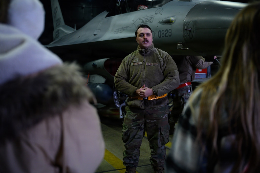 A maintenance Airman speaks about aircraft systems as spouses listen inside an aircraft shelter.