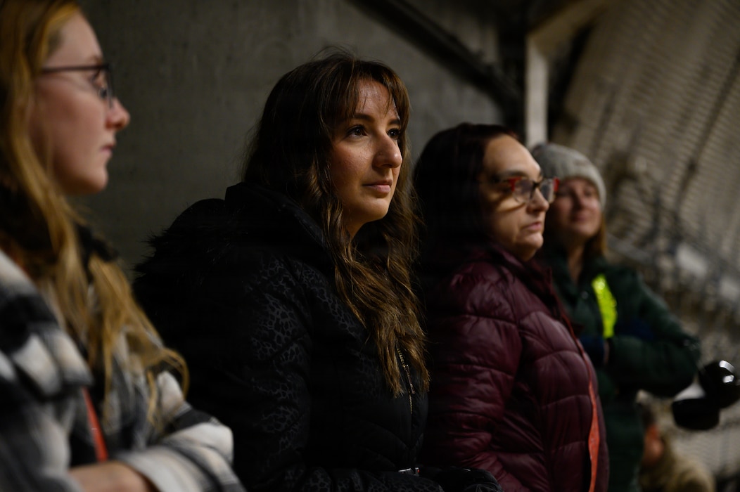 Spouses listen to a maintenance Airman inside an aircraft shelter.