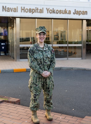 YOKOSUKA, Japan (Dec. 8, 2025) — Hospitalman Apprentice Skylar L. Foote, assigned to U.S. Naval Hospital Yokosuka, poses outside the hospital where she received the Navy and Marine Corps Achievement Medal during an awards ceremony. Foote was recognized for her life-saving response aboard a commercial flight in July, where she assessed, monitored, and coordinated care for a passenger experiencing medical distress until the aircraft landed safely. (U.S. Navy photo by Daniel Taylor/USNMRTC Yokosuka Public Affairs)