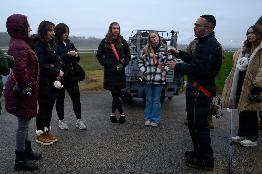 A person explains aircraft maintenance procedures to spouses on a flight line.