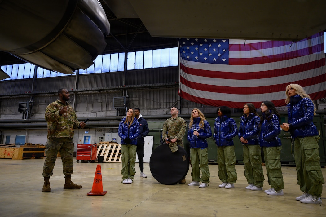 A U.S. military member talks to a group of people while standing next to a jet.