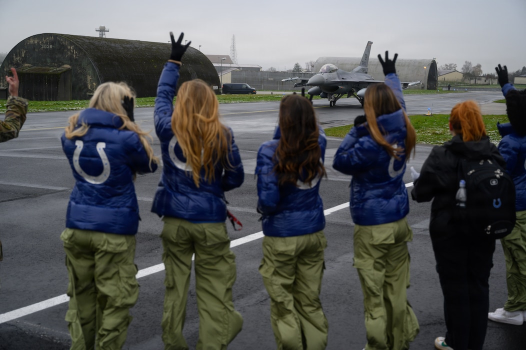 Five people watch a jet taxi on a runway.