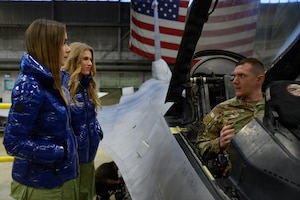 A U.S. military member sits in a plane while talking to two people.