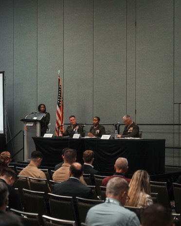 An audience observes three Marine Corps Generals participating in a panel discussion