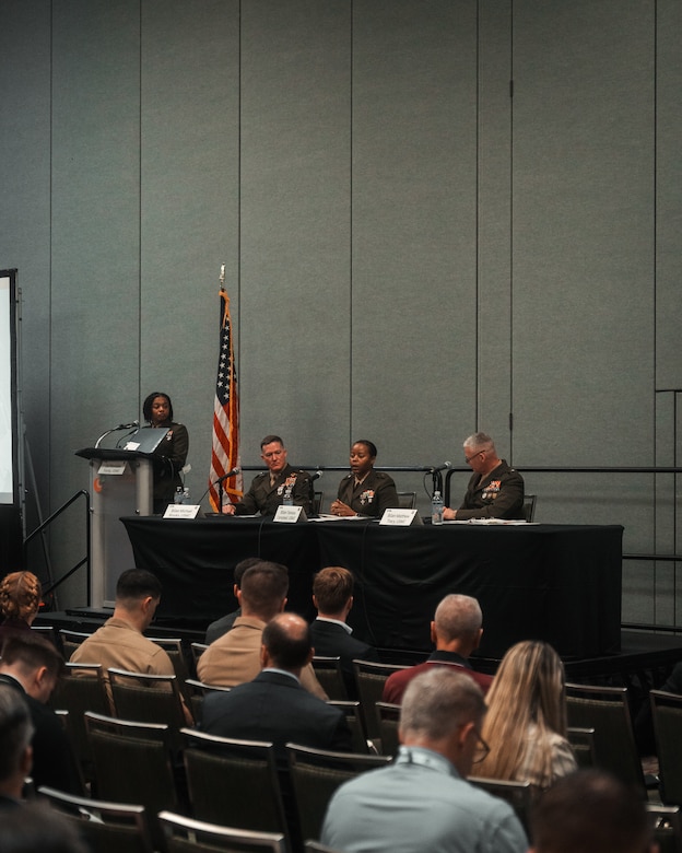 An audience observes three Marine Corps Generals participating in a panel discussion