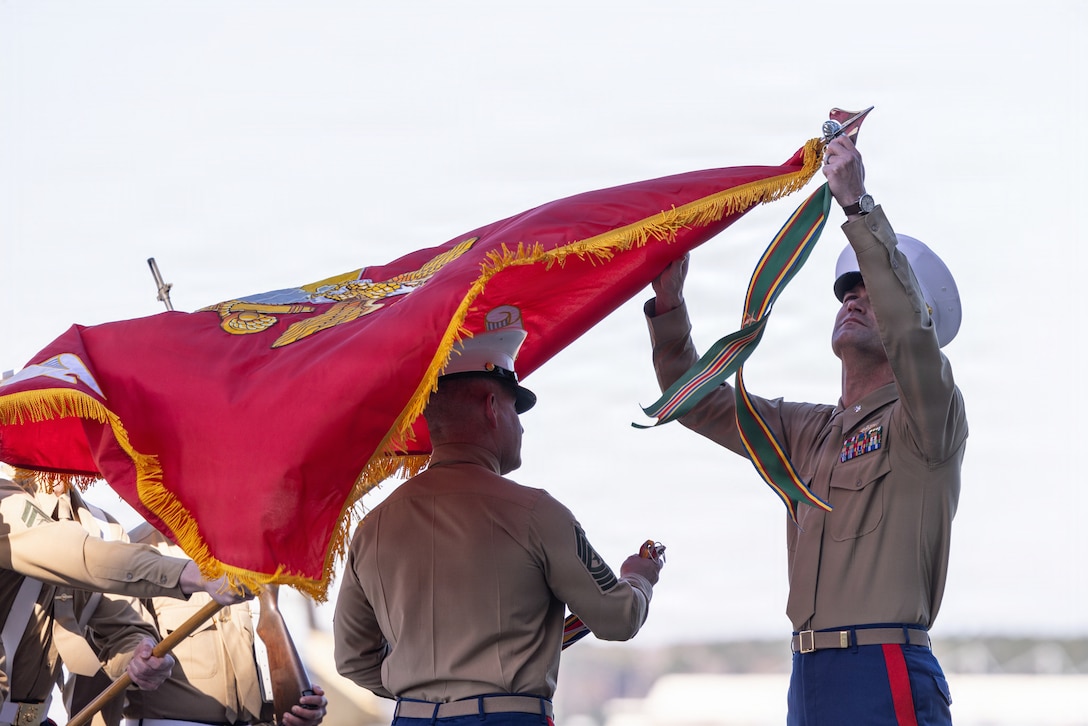 U.S. Marine Corps Sgt. Maj. Brandon L. Reagin, from South Carolina, the incoming senior enlisted leader, left, and Lt. Col. Paul J. Lancaster, from Texas, the incoming commanding officer, both with Marine Medium Tiltrotor Squadron (VMM) 264, Marine Aircraft Group 26, 2nd Marine Aircraft Wing, apply battle streamers to the organizational colors during a reactivation ceremony at Marine Corps Air Station New River, North Carolina, Dec. 11, 2025. VMM-264’s reactivation adds an additional MV-22B Osprey squadron to 2nd MAW and II Marine Expeditionary Force and reflects incremental adjustments in Force Design to meet the operational demands of the service. (U.S. Marine Corps photo by Cpl. David Ornelas Baeza)