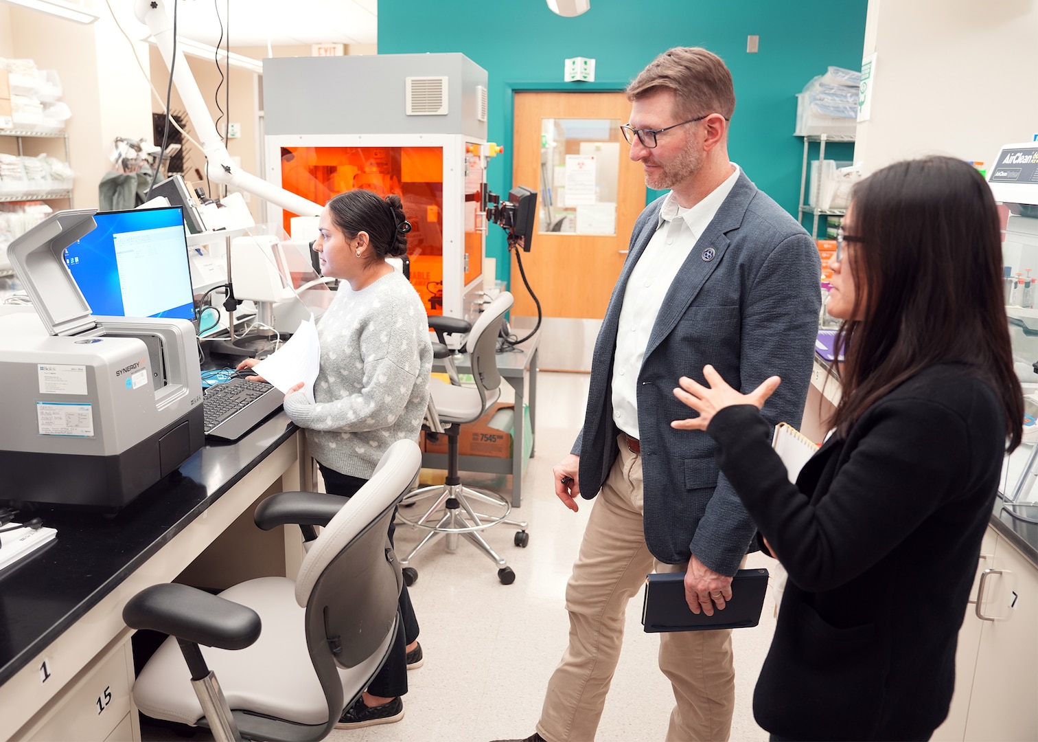 JOINT BASE SAN ANTONIO-FORT SAM HOUSTON (Dec. 8, 2025) Dr. Jeremy Pamplin, (center) program manager, Biological Technologies Office, Defense Advanced Research Projects Agency (DARPA), is briefed by research immunologist Dr. Dao Ho (right) and research scientist Phylisia Dimas, assigned to Naval Medical Research Unit (NAMRU) San Antonio on the specific methods by which NAMRU-SA assesses the viability and proliferation of living cells for DARPA’s Fieldable Solutions for Hemorrhage with bio-Artificial Resuscitation Products (FSHARP) program at the Battlefield Health & Trauma Research Institute. The FSHARP program works to develop a deployable, shelf-stable, universal whole blood substitute as a hemorrhage countermeasure to sustain injured warfighters in austere, pre-hospital settings. NAMRU San Antonio, part of Navy Medicine Research & Development, works alongside research partners in the civilian sphere, academia, industry, and other government agencies to drive support of the Department of War’s objectives for a lethal fighting force and ensures U.S. service members have access to the latest scientific advances. NAMRU San Antonio conducts gap-driven combat casualty care, craniofacial, and directed energy research in support of Navy, Marine Corps and joint U.S. warfighter health readiness and lethality while engaged in routine and expeditionary operations. (U.S. Navy photo by Burrell Parmer/Released)